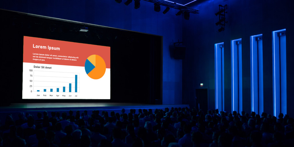 A stage in a large auditorium, in front of an audience, featuring a high‑resolution screen displaying a slide with bold colors.